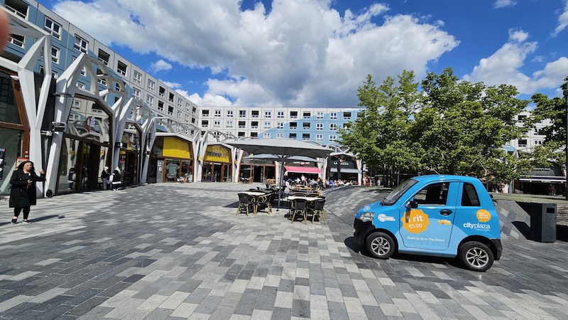 De blauwe auto van Max mobiel op het plein bij City Plaza